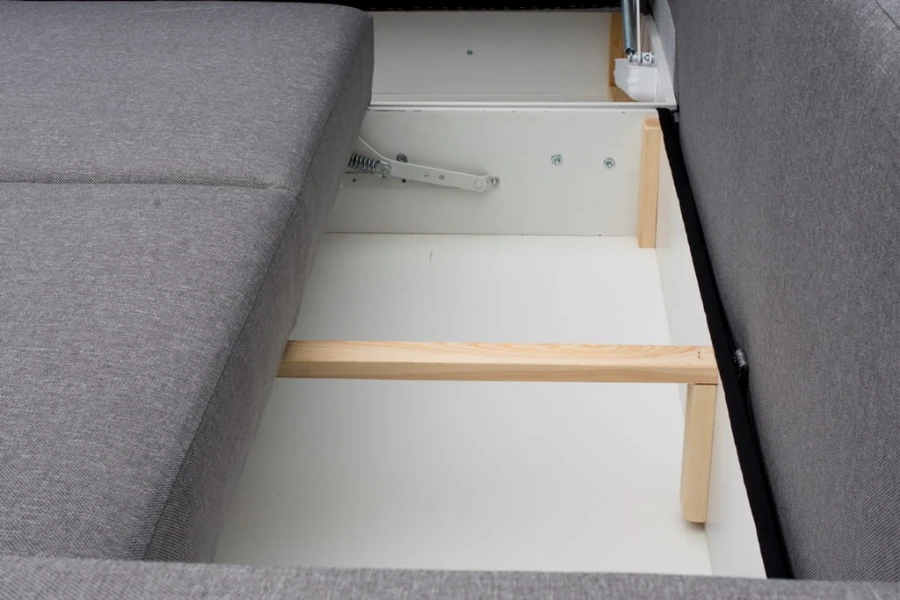 Stauraum im Bettkasten eines grauen Ecksofas mit Holzverstärkung.