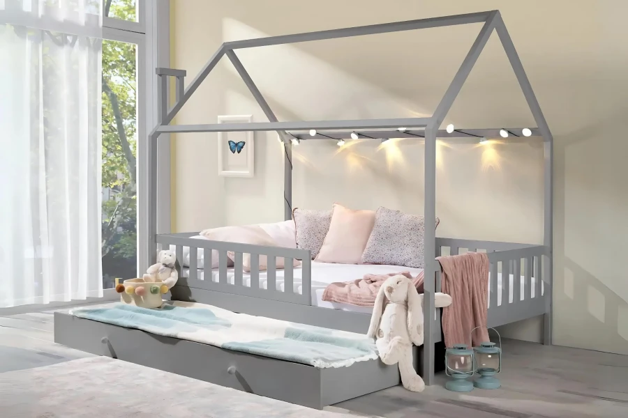Hausbett für Kinder in Grau mit Bettkasten, Kissen und Stofftieren in hellem Zimmer mit Fenster.