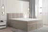 Beiges Boxspringbett mit Bettkasten ohne Bettwäsche in einem hellen Schlafzimmer.