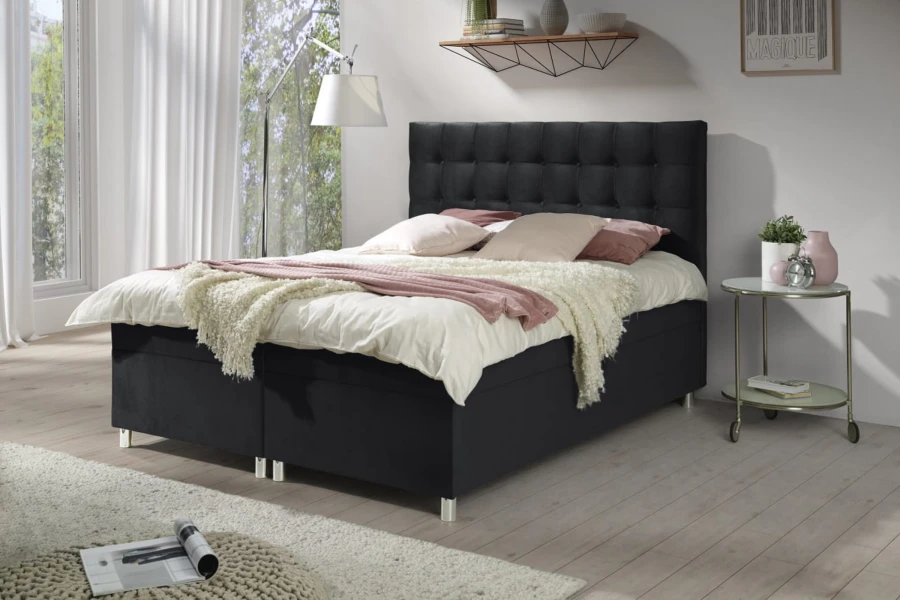 Schwarzes Boxspringbett mit hohem gepolstertem Kopfteil im hellen Schlafzimmer.