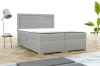 Modern grijs boxspringbed met gestoffeerd hoofdbord in een lichte slaapkameromgeving.