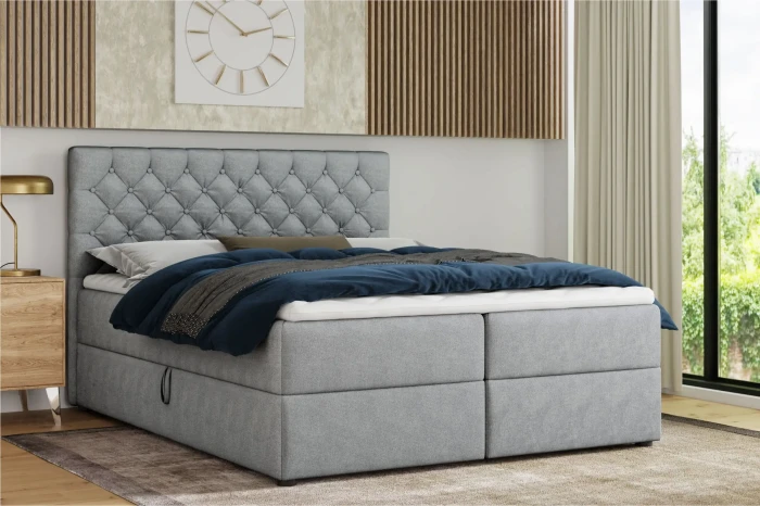 Lichtgrijs boxspringbed met gecapitonneerd hoofdbord en blauw beddengoed in een moderne slaapkamer