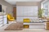 Modernes Schlafzimmer in Weiß und Eiche mit Stauraumbett, großem Schrank und gelbem Sessel.