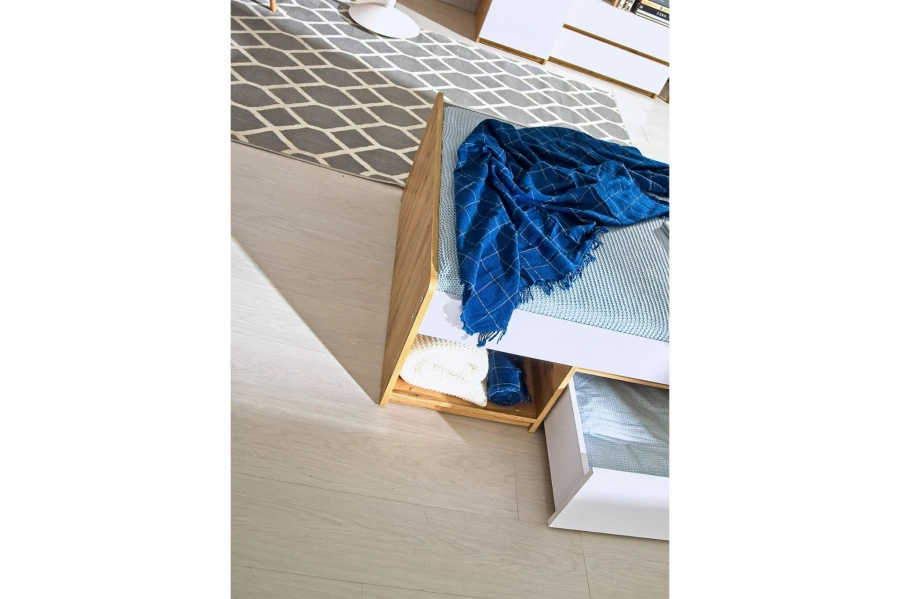 Detailansicht eines Bettes in Holzoptik mit Regalfach und blauer Decke.