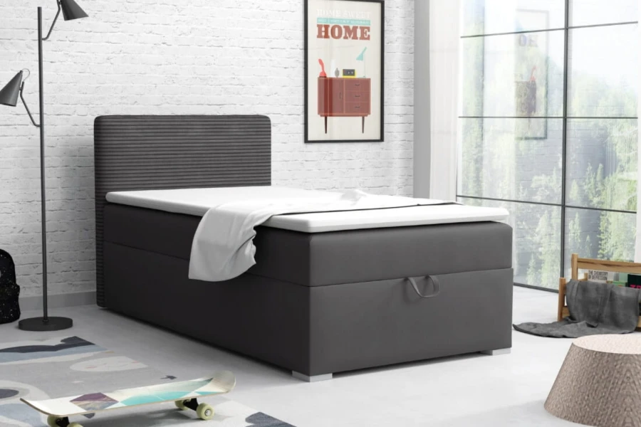 Antracietkleurig boxspringbed in een modern ingerichte kamer met bakstenen muur en raam.