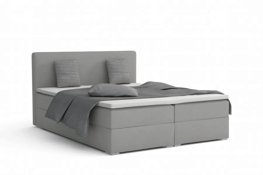 Hellgraues Boxspringbett mit grauer Tagesdecke vor weißem Hintergrund.