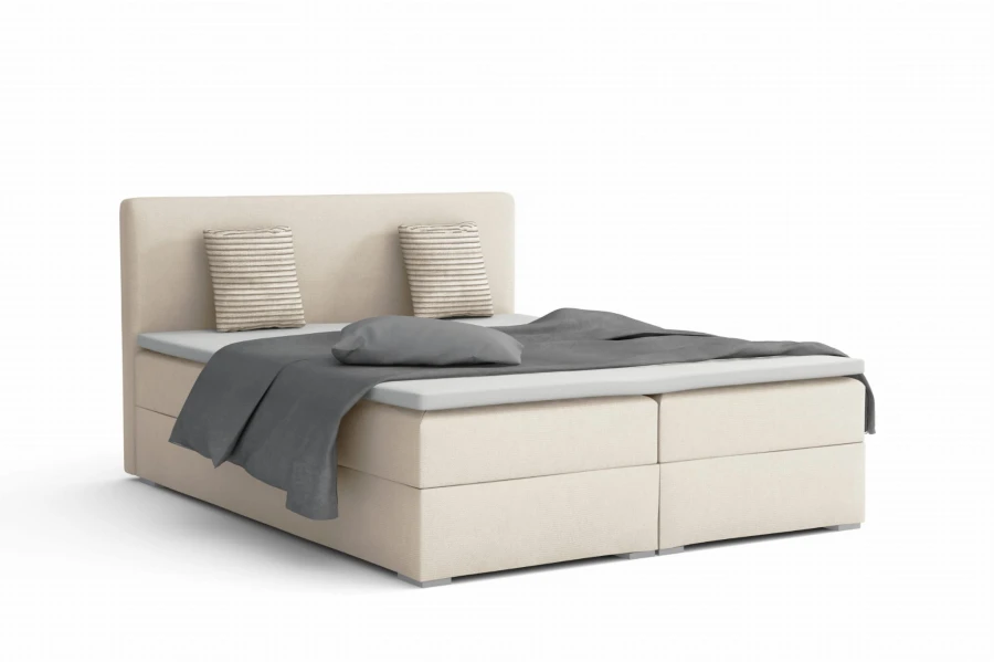 Cremefarbenes Boxspringbett mit grauen Kissen und eleganter Optik.