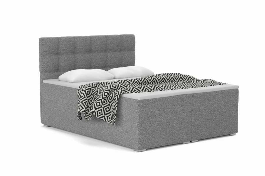 Grey boxspring bed with quilted headboard and patterned blanket on a white background.