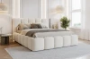 Modern wit gestoffeerd bed in bouclé-look in een lichte slaapkamer met grijs tapijt.