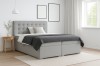 Modernes Boxspringbett in Hellgrau mit gestepptem Kopfteil in einem hellen Schlafzimmer.