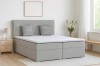 Modernes hellgraues Boxspringbett in einem hellen Schlafzimmer mit Nachttisch und Lampe.