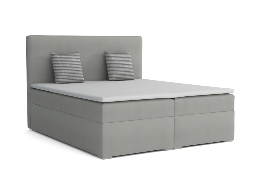 Graues Boxspringbett mit gepolstertem Kopfteil und Dekokissen vor weißem Hintergrund.