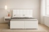 Weißes Boxspringbett mit gestepptem Kopfteil und schwarz-weißer Decke in hellem Zimmer.