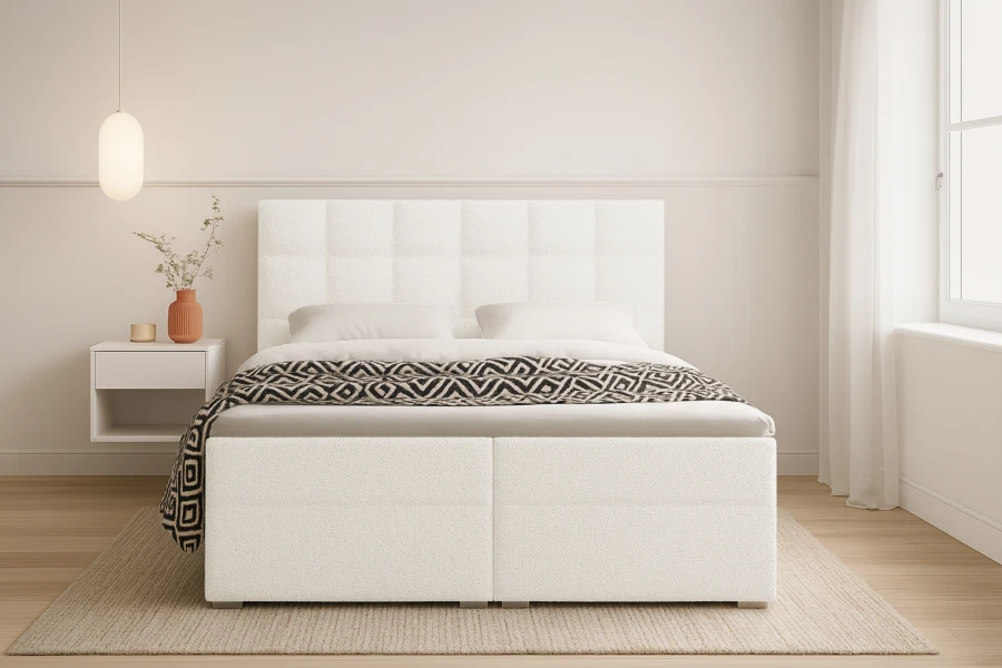 Weißes Boxspringbett mit gestepptem Kopfteil und schwarz-weißer Decke in hellem Zimmer.