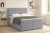 Hellblaues Boxspringbett mit gestepptem Kopfteil und schwarz-weißer Tagesdecke im Schlafzimmer.