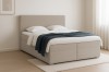 Beiges Boxspringbett aus weichem Bouclé-Stoff mit blauer Decke in minimalistischem Raumdesign.