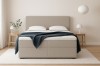 Beiges Boxspringbett mit dunkelblauer Decke im minimalistisch gestalteten Schlafzimmer.