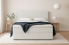 Cremefarbenes Boxspringbett mit blauer Decke und zwei hölzernen Nachttischen.