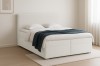 Seitenansicht eines cremefarbenen Boxspringbetts mit weißer Bettwäsche und blauer Decke.