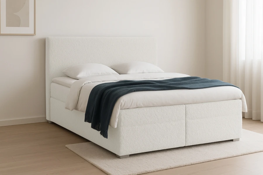 Seitenansicht eines cremefarbenen Boxspringbetts mit weißer Bettwäsche und blauer Decke.