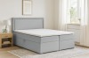 Modernes hellgraues Boxspringbett im Schlafzimmer mit hellem Holz-Nachttisch.