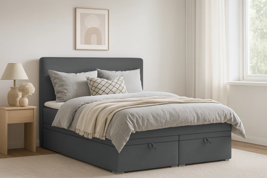 Gemütlich eingerichtetes Schlafzimmer mit grauem Boxspringbett, Kissen und Tagesdecke.