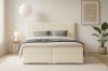 Frontalansicht eines beigen Boxspringbetts aus Cord in einem hellen, modernen Schlafzimmer.