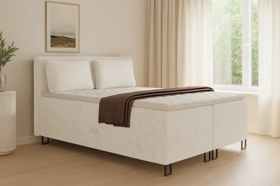 Gemütliches Boxspringbett im hellen, modernen Schlafzimmer mit Fenster und dezenter Dekoration.
