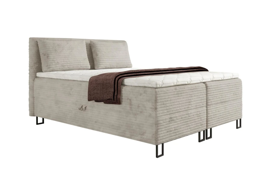 Beiges Boxspringbett in Cord-Optik mit Kissen und dekorativer brauner Decke.