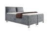 Graues Boxspringbett mit geripptem Stoff, weißem Topper und brauner Decke vor weißem Hintergrund.