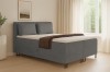 Graues Boxspringbett in hellem Schlafzimmer mit Vorhängen, Pflanze und Bild für modernes Wohnen.