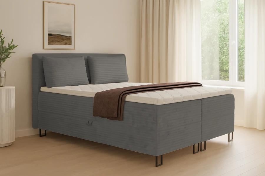 Graues Boxspringbett in hellem Schlafzimmer mit Vorhängen, Pflanze und Bild für modernes Wohnen.