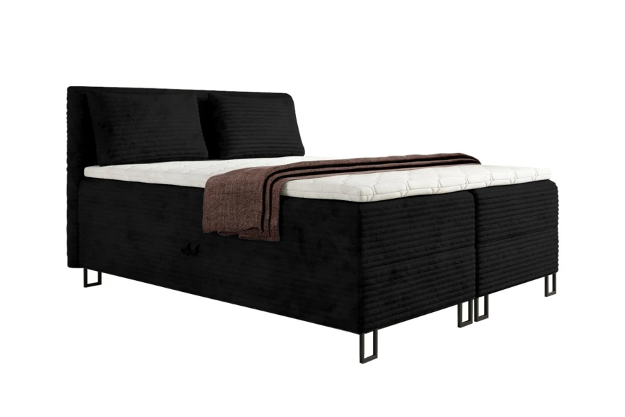 Schwarzes Boxspringbett mit geripptem Bezug, weißem Topper und brauner Decke auf weißem Grund.