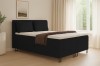 Schwarzes Boxspringbett in stilvollem Schlafzimmer mit hellen Vorhängen und Wanddekoration.