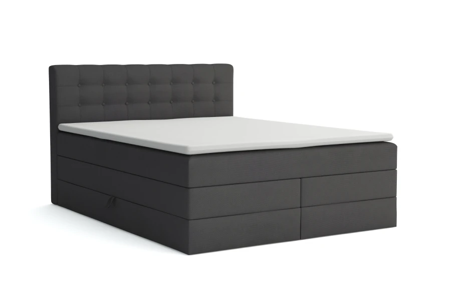 Dunkelgraues Boxspringbett mit weißem Topper und Knopfsteppung am Kopfteil vor weißem Hintergrund.