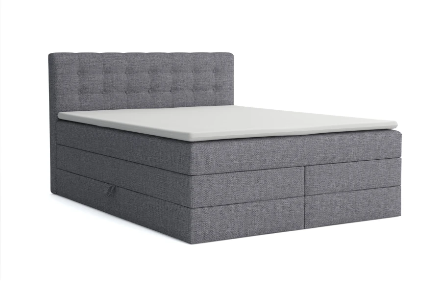 Graues Boxspringbett mit gestepptem Kopfteil und weißem Topper, isoliert auf weißem Hintergrund.