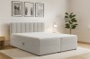 Stilvolles Schlafzimmer mit hellgrauem Boxspringbett, Zimmerpflanze und minimalistischer Wandkunst.