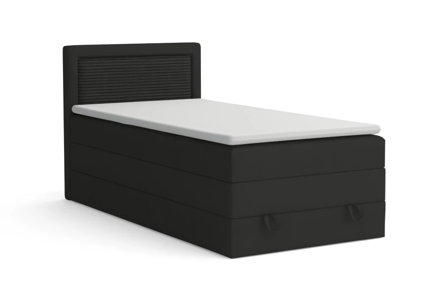 Schwarzes Boxspringbett mit weißem Topper und geriffeltem Kopfteil vor weißem Hintergrund.