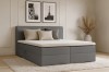 Modernes graues Boxspringbett im hellen Schlafzimmer mit dekorativen Kissen und Teppich.