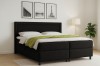 Modernes Boxspringbett in Schwarz im Schlafzimmer-Ambiente mit Stehlampe.
