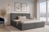 Stilvolles Schlafzimmer mit grauem Boxspringbett, moderner Stehlampe und Teppich.