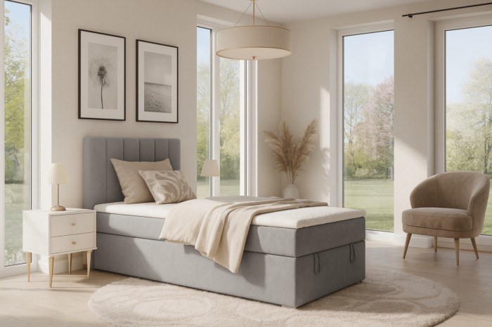 Modern grey boxspring bed in a bright bedroom with a bedside table.