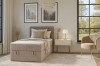Modern beige boxspringbed van corduroy-stof in een lichte slaapkamer met fauteuil en decoratie.