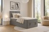 Stilvolles Schlafzimmer mit grauem Boxspringbett, Beistelltisch und Fensterfront.
