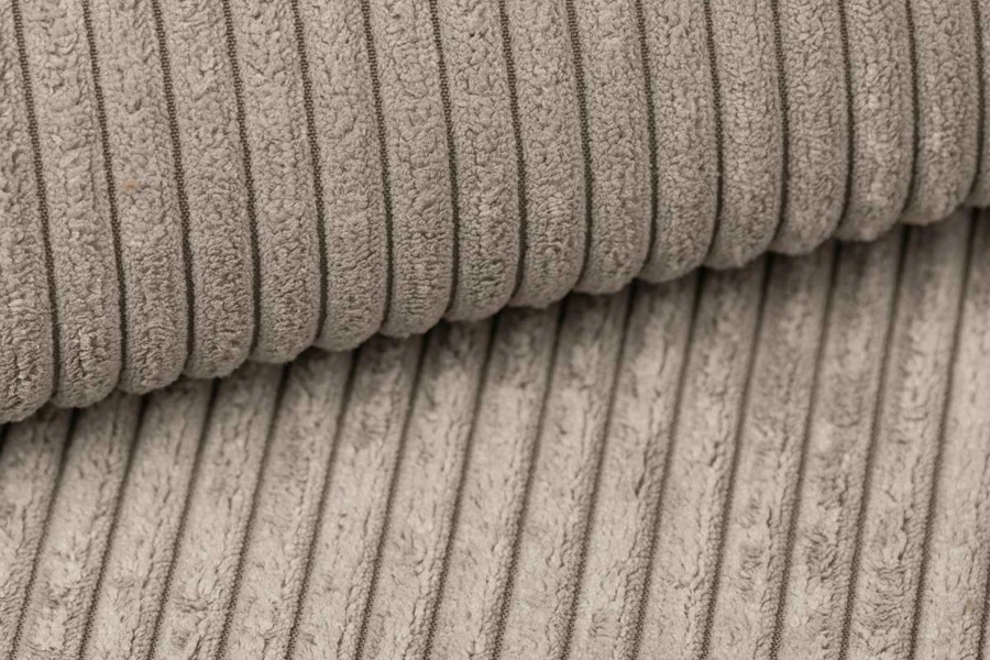Nahaufnahme der Textur: Beiger Cord-Stoff mit weicher Rippenstruktur für Polstermöbel.