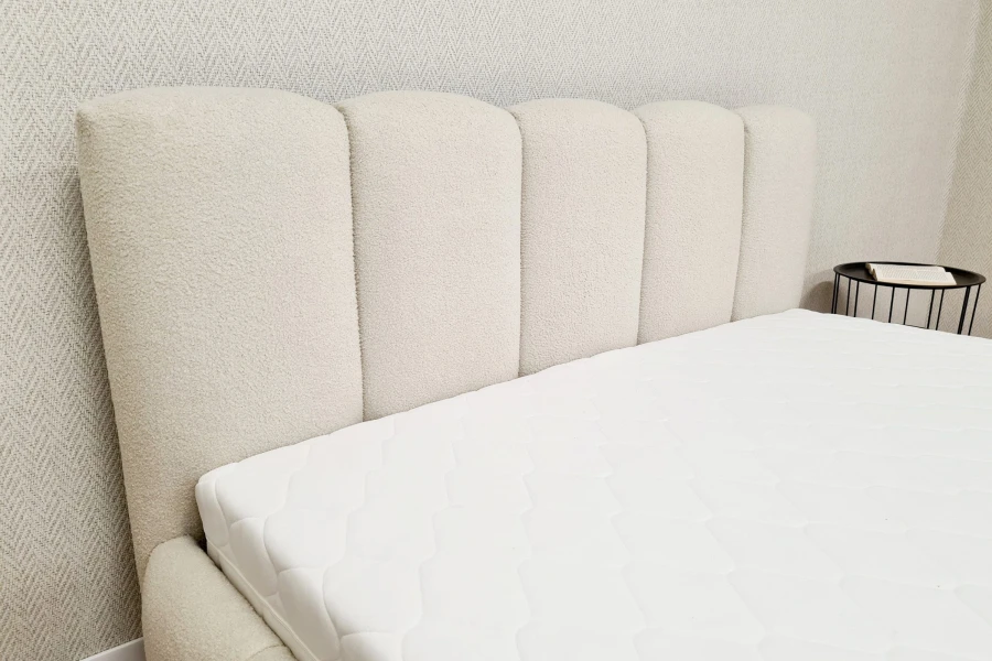 Weiße Matratze auf einem modernen Polsterbett mit weichem Kopfteil in einem hellen Schlafzimmer.