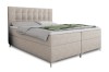 Beiges Boxspringbett mit gestepptem Kopfteil und grauer Decke auf weißem Grund.