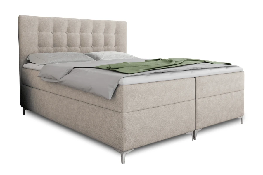 Beiges Boxspringbett mit gestepptem Kopfteil und grauer Decke auf weißem Grund.