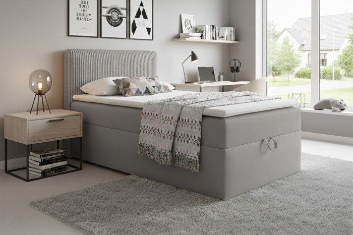 Cosy bedroom set with grey box spring bed, bedside table and modern interior design.