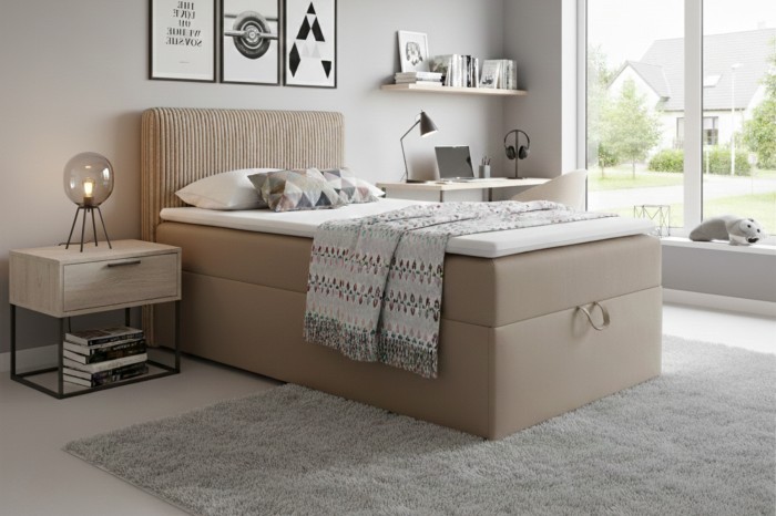 Modern beige boxspringbed met geribbeld hoofdbord in een lichte slaapkamer.